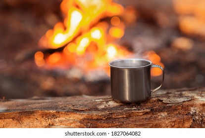 Camping Titanium Cup On Wood Over Fire Background. Lunch During Journey To The Wild. Camping Lifestyle, Copy Space