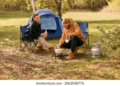 camping, tourism and travel concept - happy couple drinking beer and cooking food in pot on tourist gas burner at tent camp - Powered by Shutterstock