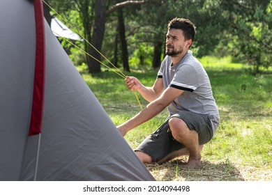 Camping, travel, tourism, hike concept - young man setting up tent in the forest.