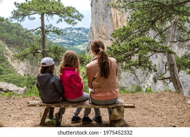 Camping, Travel, Tourism, Hike And People Concept - Children Sit On The Bench With Their Backs To Us And Look At The Beautiful Landscape In Woods