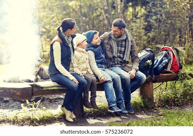 Camping, Travel, Tourism, Hike And People Concept - Happy Family Sitting On Bench And Talking At Camp In Woods