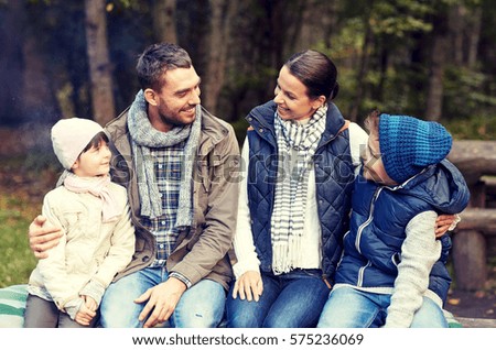 camping, travel, tourism, hike and people concept - happy family sitting on bench and talking at camp in woods