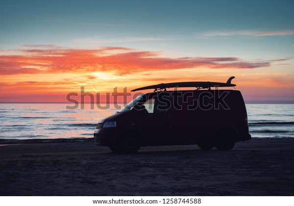 A camping van\
bus with a surf board on the roof top at the beach with summer\
sunset light. Perfect sport for a surf trip. Løkken in North\
Jutland in Denmark, Skagerrak, North\
Sea