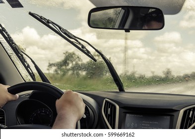 CAMPO GRANDE, BRAZIL - FEBRUARY 25, 2017: Interior Of A Moving Car On The Road On A Rainy Day With Wet Windscreen And Wiper Cleaning The Glass. Two Hands On The Wheel.