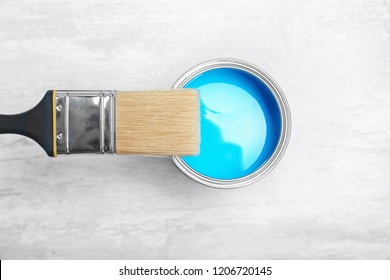Can with blue paint and brush on light background, top view