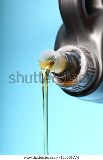 Can\
with car engine oil pouring in front  blue\
background