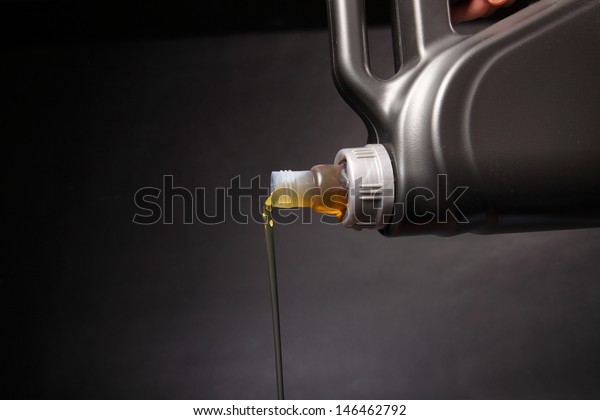 Can\
with car engine oil pouring in front black\
background