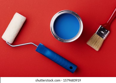 Can of classic blue paint with brush and paint roller on red background. Top view, color of year.
