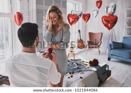 Can not believe this is happening! Surprised young woman covering face with hand and smiling while her boyfriend proposing her in the bedroom Foto stock © 