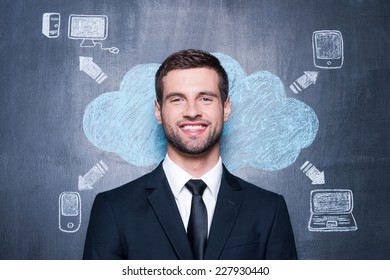 Can Not Imagine Life Without Gadgets. Handsome Young Man Smiling And Looking At Camera While Standing Against Chalk Drawing On The Blackboard