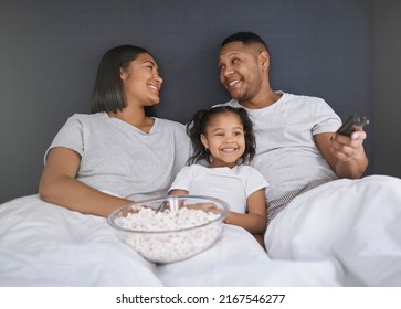 Can I Press Play Now. Shot Of A Young Couple Sitting In Bed With Their Daughter And Getting Ready To Watch A Movie.