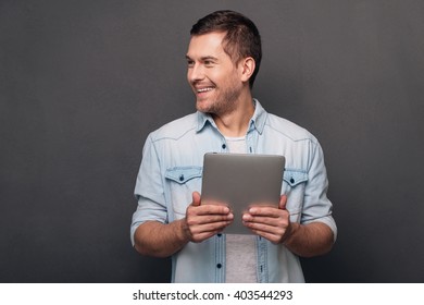 I Can Solve Your Problem! Cheerful Young Man Holding His Digital Tablet And Looking Away With Smile While Standing Against Grey Background