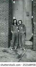 CANADA - CIRCA 1940s: Reproduction of an antique photo shows Two girls in denim overalls standing near the door of a brick industrial building
