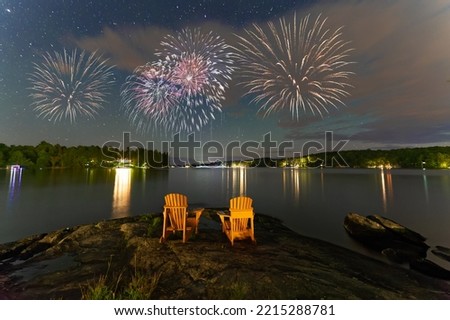 Canada Day fireworks over two Adirondack chairs  in Muskoka, Ontario Canada. The pyrotechnics are illuminating a sky full of stars