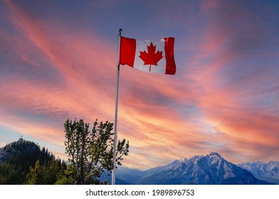 Canada flag flying atop Sulphur Mountain with sunset view of Banff National Park with Canadian Rockies in the background.