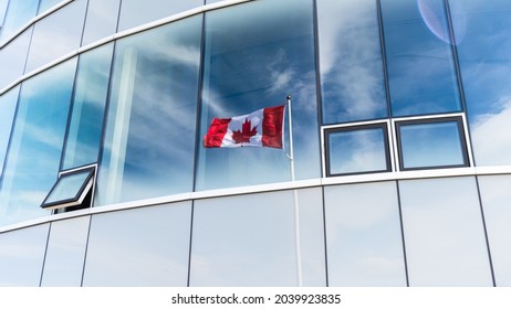 Canada Flag Waving In The Wind And Urban Skyscraper Architecture Background. Canadian Flag Pole Reflection In Glass Window From Urban Building