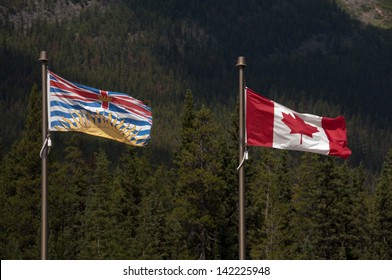 Canadian flag and British Columbia flag blowing in the wind in the Canadian alpine.