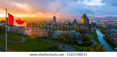 A Canadian flag flies over Old Quebec City at sunset. Aerial drone panorama view of Quebec City including Chateau Frontenac and Differin Terrace.