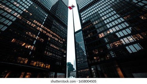 Canadian Flag On A Flag Pole Between Two Tall Buildings 