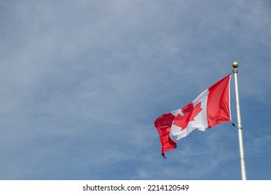 Canadian Flag On A Flag Pole Flying In The Wind Against A Blue Sky