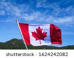 Canadian flag with red maple leaf flying in front of a blue sky
