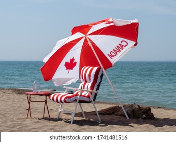 a Canadian flag umbrella and red stripped chair on the beach for Canada Day celebration 