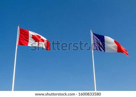 Canadian and French flags flying together against the blue sky.