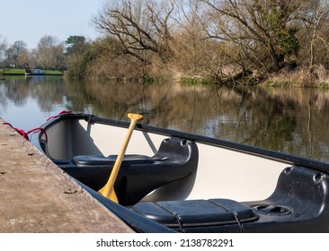 A Canadian open canoe with a paddle is tied up at a landing stage on a river on a sunny day - Shutterstock ID 2138782291