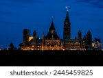 Canadian Parliament at night in Ottawa, Canada.  The Canadian flag is brightly illuminated at the top of the Peace Tower. 