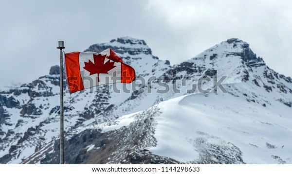 Canadian\
Rockies - A Canadian National Flag flying at front of two\
snow-covered high mountain peaks, Columbia Icefield Discovery\
Centre, Jasper National Park, Alberta,\
Canada.