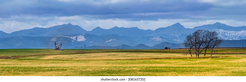 Canadian Rocky Mountain Range Beautiful Rural Alberta Prairies And Grassland Panoramic Landscape. Oil Pump Jack In Farmland