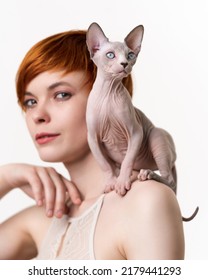 Canadian Sphynx Cat Sitting On Shoulder Of Redhead Young Woman With Short Hair. Selective Focus On Cat, Shallow Depth Of Field. Head Shot On White Background. Part Of Series.