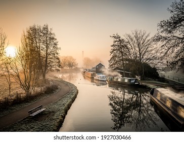 Canal narrow river boats at foggy dawn sunrise with beautiful mist orange haze wood burning smoke from chimneys silhouette trees with sun behind rising