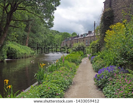 a canal path surrounded by summer flowers with a row of old stone houses at eastwood in hebden bridge west yorkshire