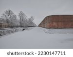 A canal and a red brick fortress in the city of Kronstadt against the background of winter trees in cloudy weather