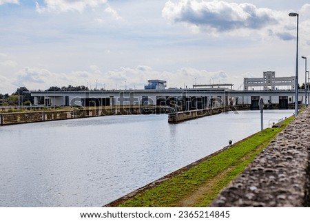 Canal towards Lanaye lock complex with closed floodgates, Albert canal, construction walls, vehicular bridge in background against misty sky, sunny summer day in Ternaaien, Belgium
