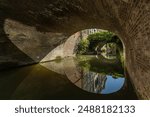 Canal Utrecht under a bridge with reflections of several bridges covered in plants. Wide angle view.