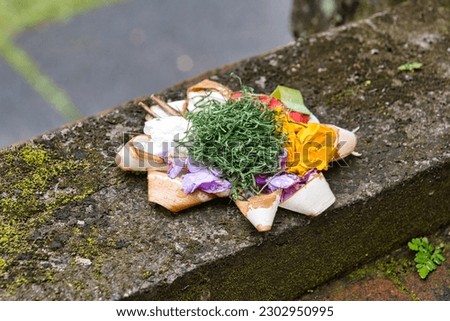 Canang Sari, Balinese offerings on a stone wall. Balinese people provide offerings. Little flower basket in Bali, Indonesia as offering to their gods. Small religions offering made out of flowers. 