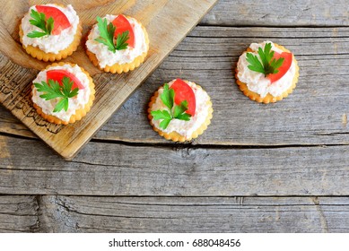 Canape cooked from salty crackers with spicy soft cheese, tomato slice and green parsley leaf. Spicy cheese canape on an old wooden background. Quick aperitif recipe. Top view - Powered by Shutterstock