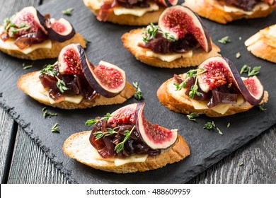Canape or crostini with toasted baguette, cheese, onion jam, figs and fresh thyme on a slate board. Delicious appetizer, ideal as an aperitif. Selective focus