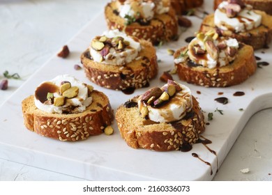 Canape or crostini with toasted baguette, goat cheese, reduced balsamic, toasted pistachio nuts and fresh thyme on a white marble board. Delicious appetizer, ideal as an aperitif. Selective focus - Powered by Shutterstock