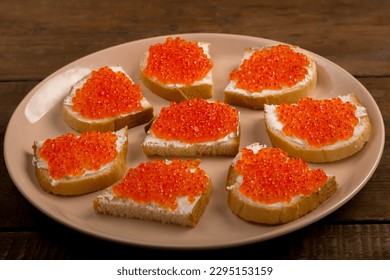 Canape with red caviar in butter on a beige plate. Horizontal photo.