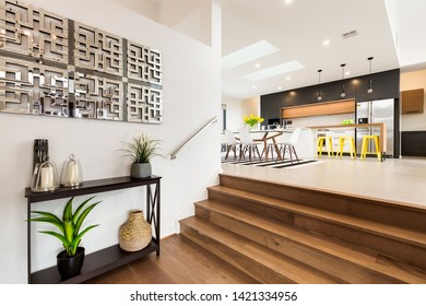 CANBERRA, AUSTRALIA – JUNE 6, 2018: Looking From The Stairway To A Spacious Kitchen Furnished With Chairs, Table, Sink, Island, Stools, Wall Stove And Large Fridge In A Modern Home