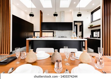 CANBERRA, AUSTRALIA – MAY 18, 2018: Closeup Of A Kitchen Table Setting Looking Toward A Spacious Kitchen With The Island Straight Ahead And Sink And Faucet To The Right In A Modern Home
