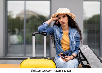 Canceled or delayed flight, difficulties while travelling. Upset young woman tourist waiting for flight at airport, holding documents, phone, touching her head, feeling stressed, looking at copy space