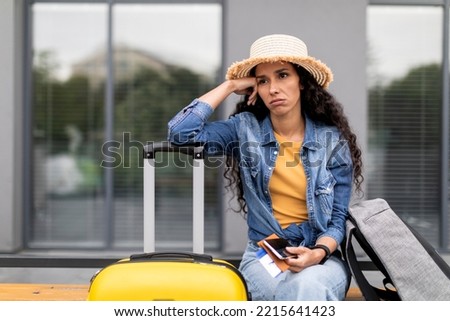 Canceled or delayed flight, difficulties while travelling. Upset young woman tourist waiting for flight at airport, holding documents, phone, touching her head, feeling stressed, looking at copy space Foto stock © 