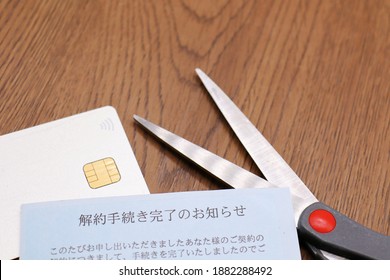 A Cancelled Credit Card Is Cut With Scissors. Documents In Japanese. Translation: Notice Of Completion Of Cancellation, Completed For Your Contract Offered.