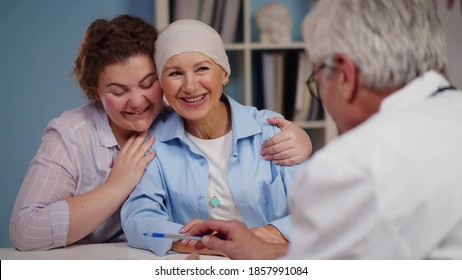 Cancer Patient Woman Visiting Doctor With Daughter And Smiling Hearing Good News. Oncologist Telling Good News About Recovery To Senior Female Patient And Her Daughter