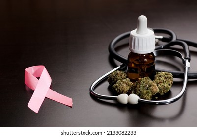 cancer pink ribbon with medical marijuana buds, stethoscope, oil bottle, brown background.