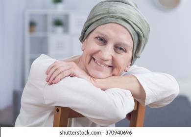 Cancer woman with headscarf sitting on chair, smiling